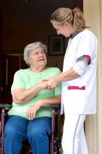 Pflegerin reicht Patientin im Rollstuhl die Hand