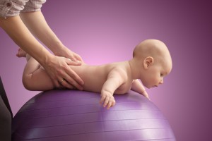 Woman is doing massage her baby on a purple ball. Color background.